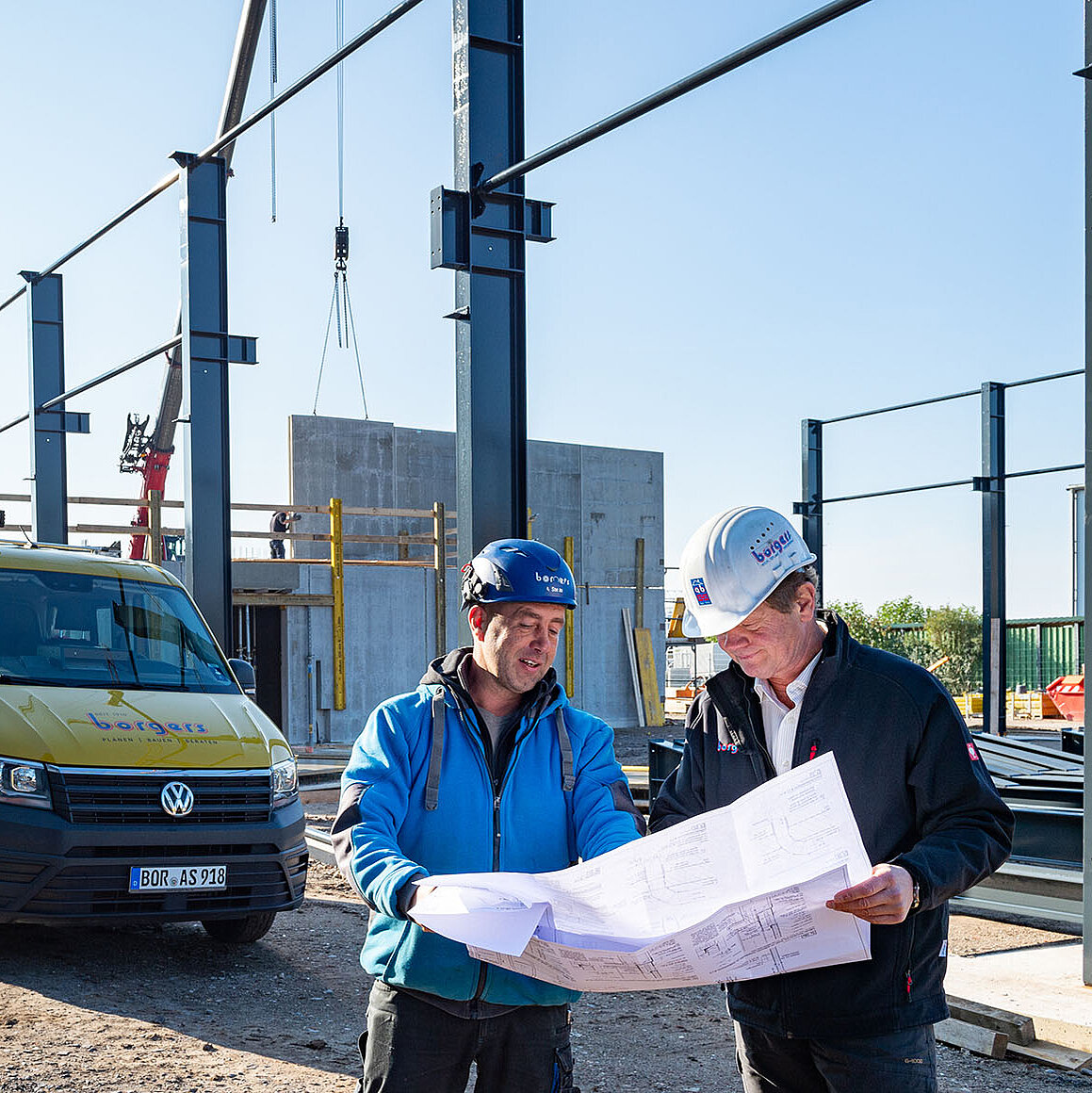 Zwei Mitarbeiter blicken auf der Baustelle auf einen Plan