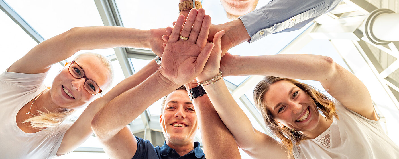 Vier Mitarbeitende stehen im Kreis und legen die Hände übereinander