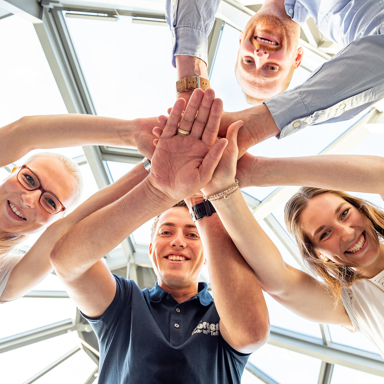 Vier Mitarbeitende stehen im Kreis und legen die Hände übereinander